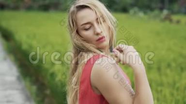 一个年轻的金发女郎站在稻田里，把脸转到镜头里，用手<strong>开始表演</strong>舞蹈